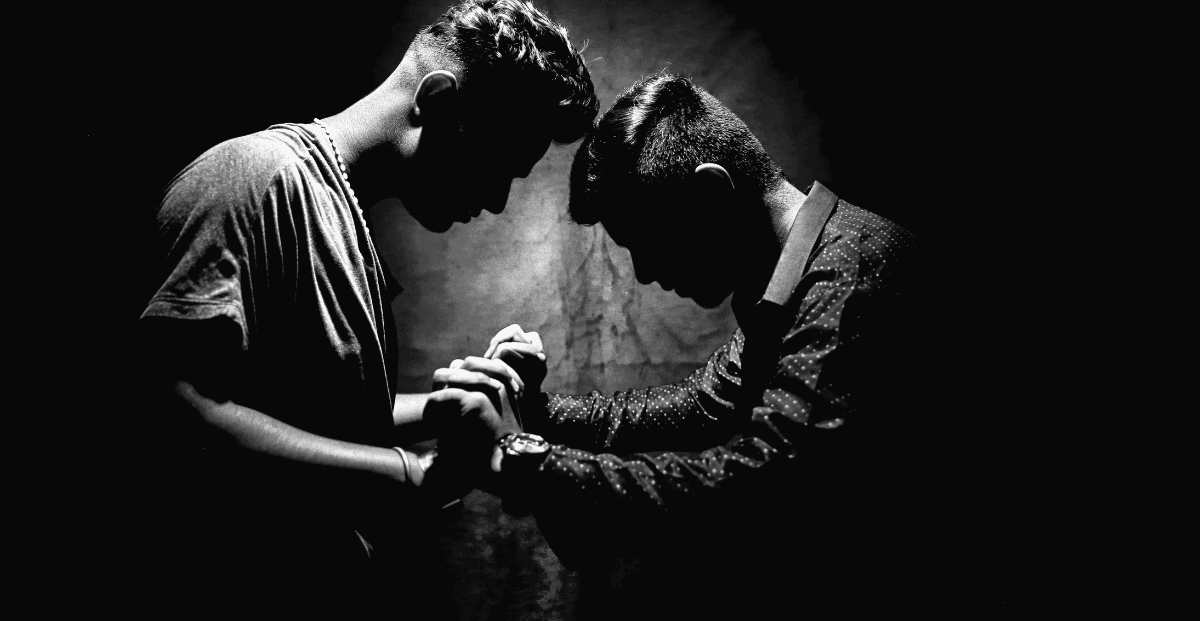 Dois homens um de frente para o outro de mãos dadas orando.