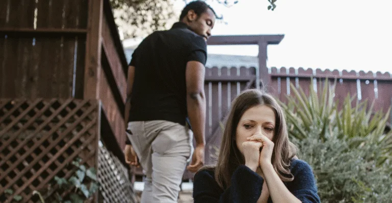 Uma mulher triste sentada e um homem com semblante nervoso subindo a escada.